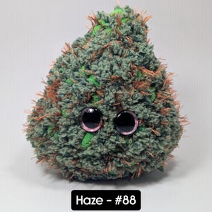 May include: A plush, green and brown, teardrop-shaped creature with large, black eyes and pink accents. The soft toy has a textured, fuzzy appearance. The text "Haze - #88" is displayed in a black rectangle at the bottom.