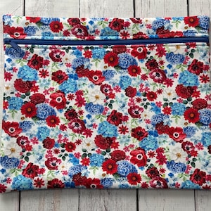 May include: A white zippered pouch with a floral print featuring red, blue, and white flowers. The pouch has a blue zipper and a small white tag with text.