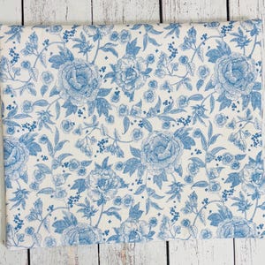 May include: A rectangular fabric item with a repeating floral pattern in light blue and white. The design features large peony blooms and smaller floral accents, creating a classic, elegant aesthetic. The fabric is likely cotton or a similar material.