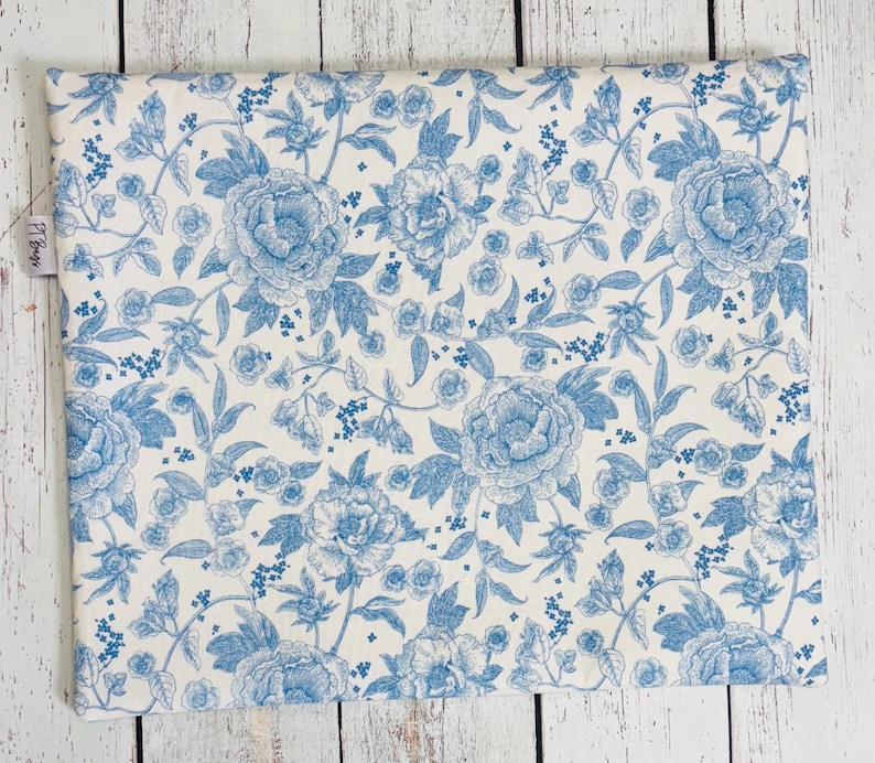 May include: A rectangular fabric item with a repeating floral pattern in light blue and white. The design features large peony blooms and smaller floral accents, creating a classic, elegant aesthetic. The fabric is likely cotton or a similar material.