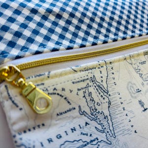 May include: Close-up of a fabric pouch with a blue and white gingham pattern on top and a map print on the bottom. A gold zipper runs across the middle. The map shows the Mid-Atlantic region.