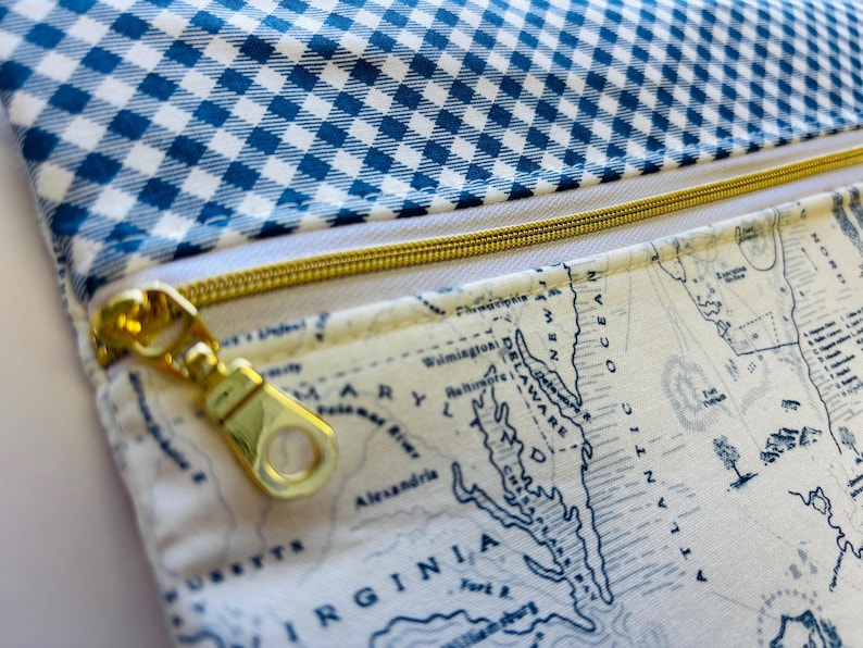 May include: Close-up of a fabric pouch with a blue and white gingham pattern on top and a map print on the bottom. A gold zipper runs across the middle. The map shows the Mid-Atlantic region.