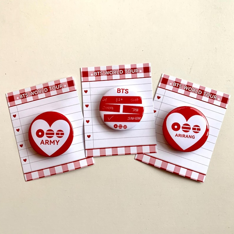 May include: Three red and white pinback buttons with the text "BTS WORLD TOUR" on the top. Two buttons have a heart design with the text "ARMY" and "ARIRANG". The third button has the text "BTS" and other names.