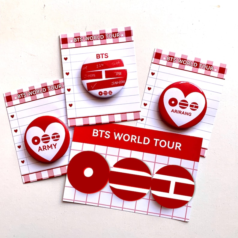 May include: A collection of red and white BTS World Tour buttons and cards. The buttons feature the BTS logo, names, and heart designs. The cards have a grid pattern and the text "BTS WORLD TOUR".