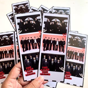 Pode incluir: Uma coleção de tiras fotográficas retangulares com o grupo BTS. Cada tira contém três imagens empilhadas dos sete membros em várias roupas, com ilustrações de corações vermelhos e o texto BTS WORLD TOUR ARIRANG impresso na parte inferior.