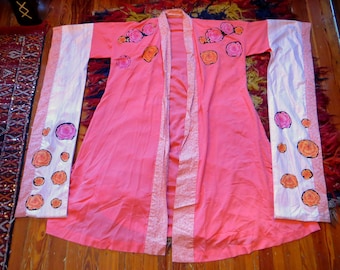 May include: A coral-colored robe with long sleeves and a floral pattern. The sleeves are white with pink and orange flower designs. The robe has a matching floral trim along the edges and a tie closure.
