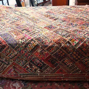May include: A large, rectangular, multi-colored quilt with a patchwork design. The quilt features a variety of colors including red, purple, and gold. The quilt is placed on a bed and has a decorative border.