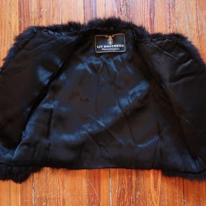 May include: Black fur vest with a satin lining. The vest has a label that reads "LIT BROTHERS Philadelphia". The fur appears to be in good condition. The vest is open, showing the interior lining.