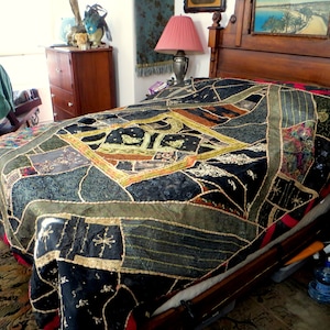 May include: A patchwork quilt with a variety of fabrics in shades of black, green, brown, and red covers a bed. The quilt features a geometric design with embroidered details and decorative stitching. The bed has a dark wooden headboard and frame.