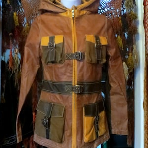 May include: A brown leather jacket with a hood, multiple pockets, and a belt. The jacket features a zipper closure and contrasting orange and brown accents. The pockets have buckle closures. The jacket is displayed on a mannequin.