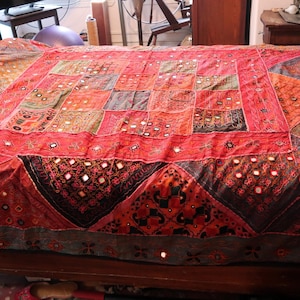 May include: A red and black patchwork quilt with intricate patterns and mirrored accents. The quilt is spread across a wooden bed frame, showcasing a blend of textures and colors. The design features geometric shapes and a vintage aesthetic.