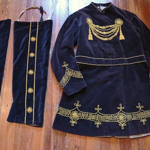 May include: A dark navy blue velvet costume with gold embroidery. The ensemble includes a long-sleeved tunic, two leg coverings, and a carrying strap. The tunic features ornate gold embellishments on the chest, sleeves, and hem.