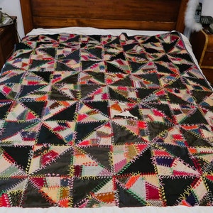 May include: A handmade quilt with a patchwork design. The quilt features a pattern of black, gray, and colorful triangular patches, stitched together with contrasting thread. The quilt is spread across a bed.