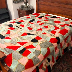 May include: A patchwork quilt in shades of red, pink, black, gray, and light blue covers a wooden bed. The quilt features geometric shapes and a vintage aesthetic, perfect for a bedroom.