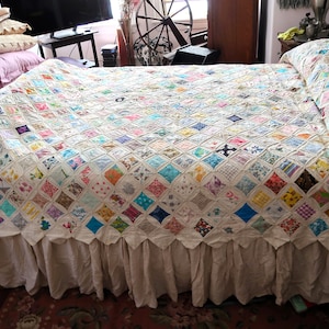 May include: A handmade quilt with a diamond pattern in various colors, including blue, pink, and green. The quilt is on a bed with a white bed skirt. The overall theme is vintage and home decor.