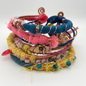 Peut inclure: Une pile de bracelets en tissu coloré enroulés de fil de cuivre et de perles turquoise.