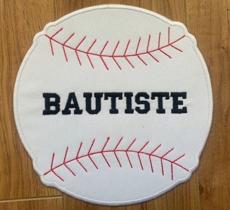 May include: White baseball-shaped patch with red stitching and the name "BAUTISTE" embroidered in black.