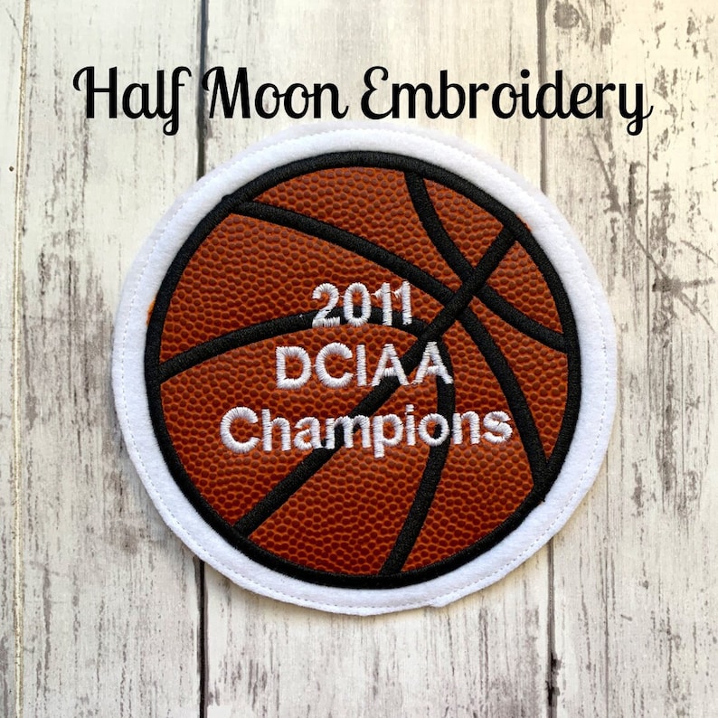 May include: A white and brown embroidered patch of a basketball with the text "2011 DCIAA Champions" in white.