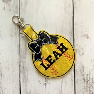 May include: Yellow softball keychain with a black bow and the name "LEAH" embroidered on it.