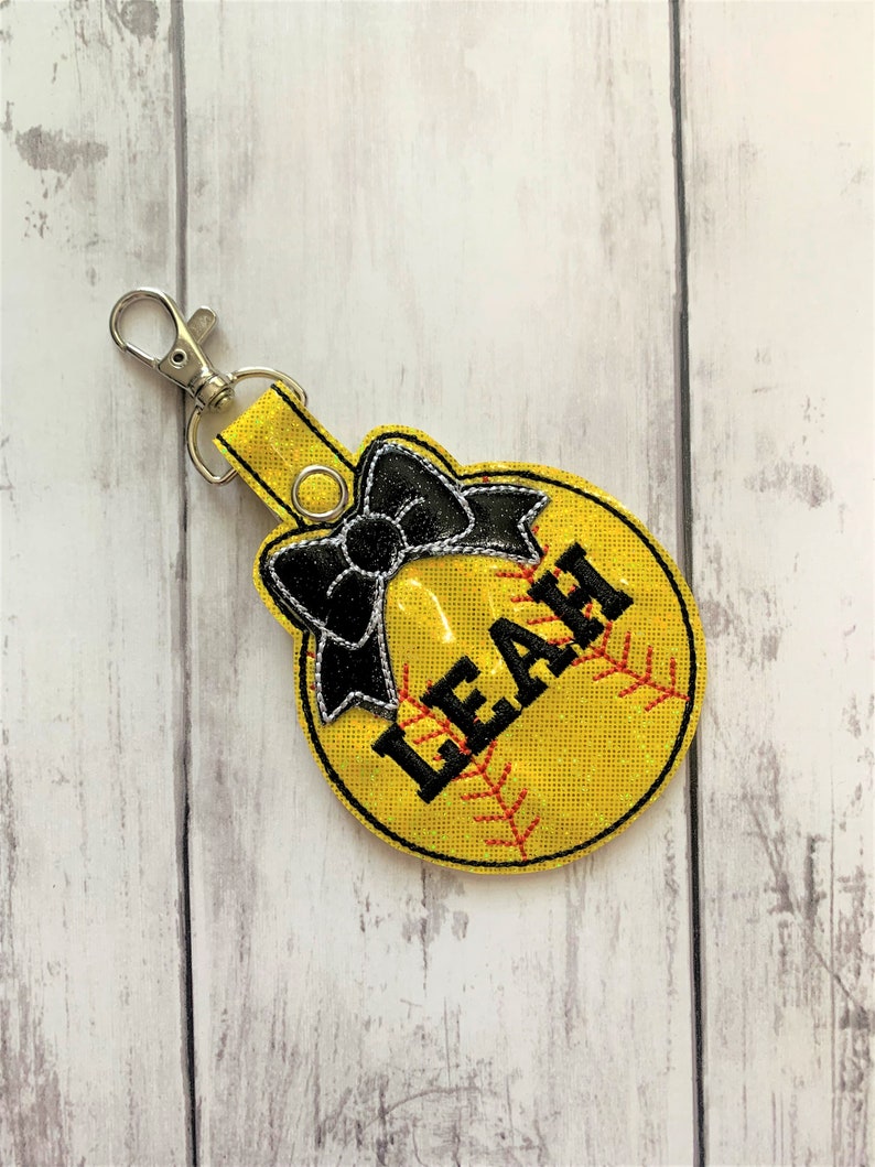 May include: Yellow softball keychain with a black bow and the name "LEAH" embroidered on it.