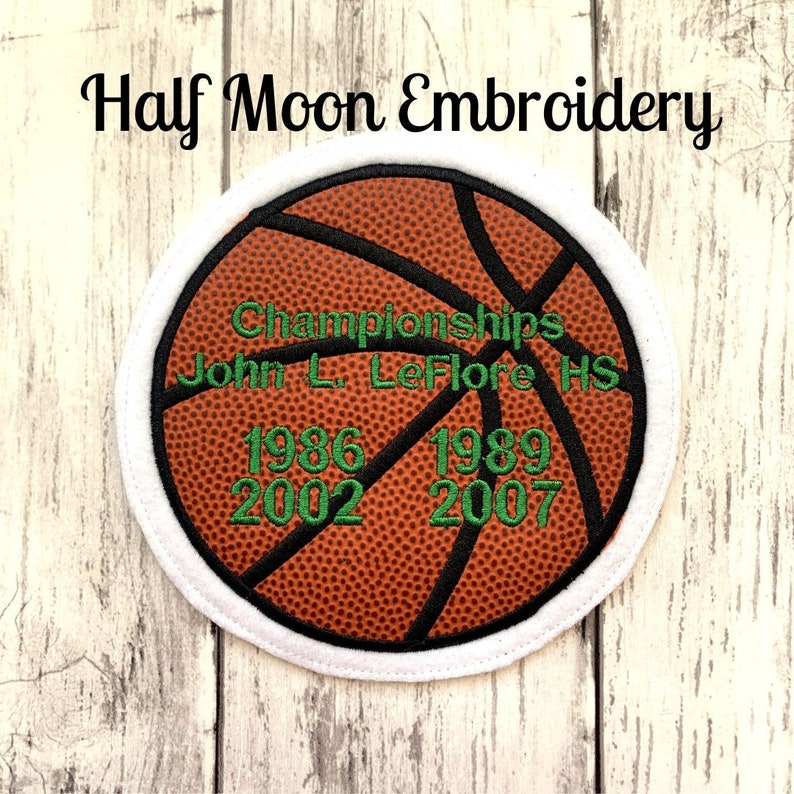 May include: A brown and black basketball with white stitching. The basketball has green text that reads "Championships John L. LeFlore HS 1986 1989 2002 2007".