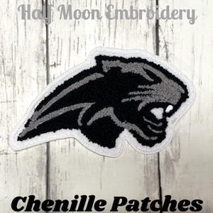 May include: A black and grey chenille patch in the shape of a panther's head with a white border. The text "Half Moon Embroidery" is at the top, and "Chenille Patches" is at the bottom.