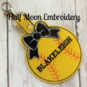 May include: Yellow softball keychain with black stitching and a black bow. The softball has the name "BLAKELY" embroidered on it.