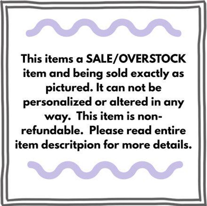 May include: A square sign with a dark gray border and light purple wavy lines at the top and bottom. The text reads: This items a SALE/OVERSTOCK item and being sold exactly as pictured. It can not be personalized or altered in any way.