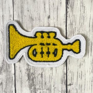 Peut inclure: Un écusson brodé jaune en forme de trompette avec une bordure blanche épaisse. Le motif de la trompette présente un large pavillon à gauche, trois pistons au centre et une embouchure à droite, le tout souligné par un fil noir.