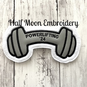 May include: A gray and black embroidered patch shaped like a dumbbell with the text "POWERLIFTING '24" on it.