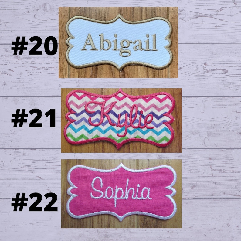 May include: Three embroidered name patches. The top patch is light blue with the name "Abigail" in gold thread. The middle patch has a chevron pattern with the name "Kylie" in pink. The bottom patch is pink with the name "Sophia" in white.