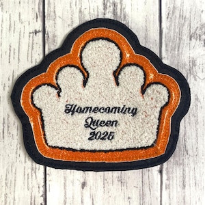 May include: A crown-shaped patch featuring a white textured center with the black embroidered text Homecoming Queen 2025. The design is outlined by a vibrant orange glitter border and a solid black outer edge, creating a layered appearance.