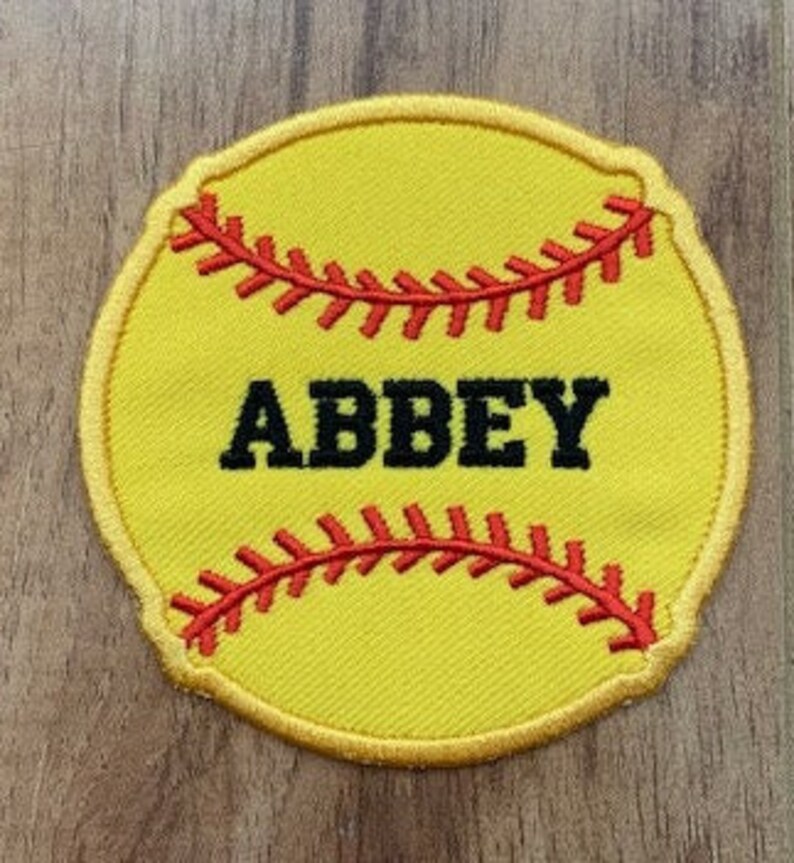 May include: Yellow softball patch with red stitching and black outline. The word "ABBEY" is embroidered in black on the patch.