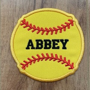 May include: Yellow softball patch with red stitching and the name "ABBEY" in black text.