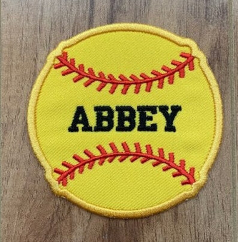 May include: Yellow softball patch with red stitching and the name "ABBEY" in black text.