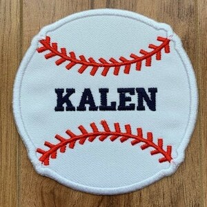 May include: White baseball-shaped patch with red stitching and the name "KALEN" embroidered in navy blue.