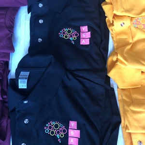 May include: Two black polo shirts with a colorful brain graphic and the letters YSA embroidered on the right chest. The shirts are folded and stacked on a white surface.