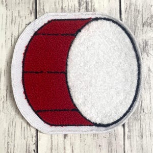 May include: A circular embroidered patch featuring a textured red section on the left with horizontal black stitching lines and a large, textured white circular section on the right, all bordered by a white fabric edge and a thin black outline.