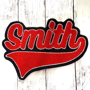 May include: A custom tufted rug featuring the name Smith in bold red script lettering with a white outline, set against a solid black background. The design includes a prominent red swoosh tail extending from the letter h across the bottom.