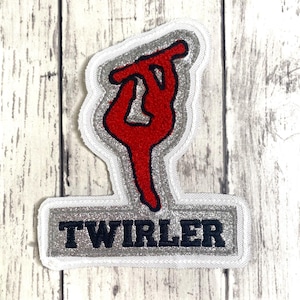 May include: A fabric patch featuring a red silhouette of a person performing a baton twirling move. The design is outlined in silver glitter fabric with a white border. Below the figure, a silver glitter rectangular base displays the word TWIRLER.