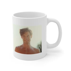 Puede incluir: Taza de cerámica blanca con una fotografía de una persona sonriente. La imagen está sobre un fondo suave y borroso. La taza tiene un asa estándar y un acabado brillante, adecuada para bebidas frías o calientes.
