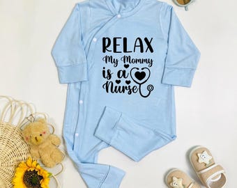 May include: A light blue baby onesie with long sleeves and snap closures. The onesie features the text "RELAX My Mommy is a Nurse" in black script, along with a heart and stethoscope graphic. Other items include sunglasses, shoes, a teddy bear, and a sunflower.