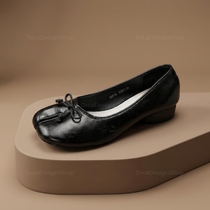 May include: A black leather ballet flat with a split-toe design, featuring a small decorative bow on the front and a low block heel. The interior lining is white, and the inner sole is printed with the text 189-6 235(1.5).