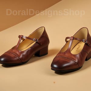 Peut inclure: Une paire de chaussures Mary Jane en cuir marron avec une bride en T et une fermeture à boucle. Les chaussures ont un bout arrondi et un petit talon bloc. L'image comprend le texte "DoralDesignsShop".