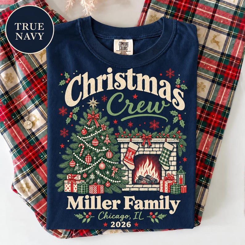 May include: A navy blue t-shirt featuring a graphic of a decorated Christmas tree, a fireplace with two stockings, and wrapped gifts. The text reads Christmas Crew, Miller Family, Chicago, IL, and 2026. A circular label in the corner says True Navy.