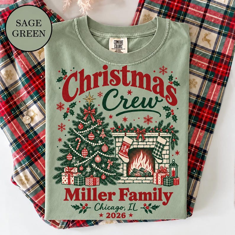 May include: A sage green t-shirt featuring a graphic with the text Christmas Crew, Miller Family, Chicago, IL, 2026. The design includes a decorated Christmas tree, a fireplace with stockings, and wrapped gifts in red, white, and green colors.