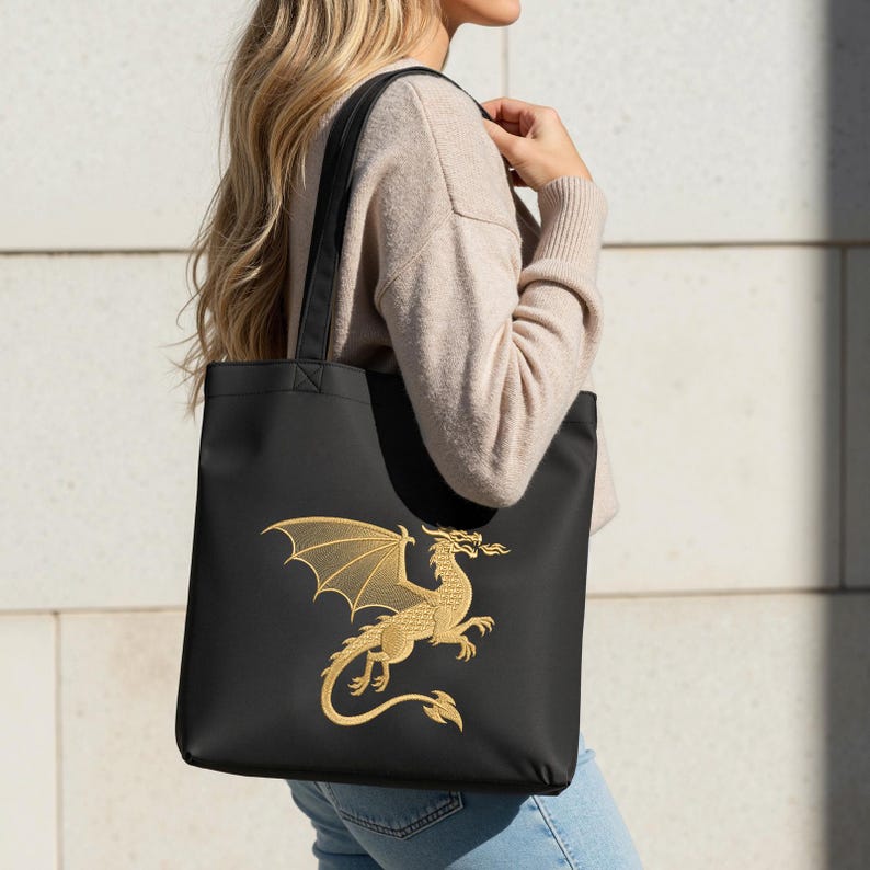 May include: Black tote bag featuring a gold embroidered dragon design. The dragon has outstretched wings and a fiery breath. The bag has black handles and is carried over the shoulder.