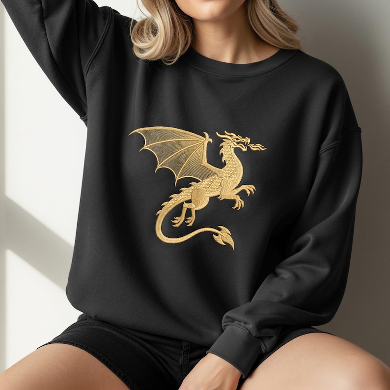 May include: Black sweatshirt featuring a gold embroidered dragon design. The dragon is depicted with outstretched wings and a fiery breath, creating a striking contrast against the dark fabric. A stylish and comfortable garment.