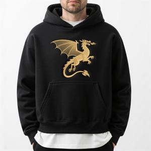 May include: Black hooded sweatshirt with a gold dragon graphic on the front. The dragon is depicted with outstretched wings and flames. The sweatshirt has a kangaroo pocket and a drawstring hood.
