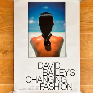 Peut inclure: Une affiche d'exposition rectangulaire intitulée David Bailey's Changing Fashion, présentant la photographie du dos d'une personne face à la mer et au ciel bleu. Le texte indique A Coruña Spain, les dates 28 juin 2025 - 14 sept 2025 et le site web.